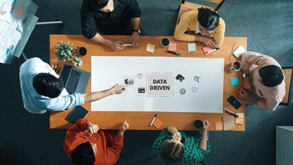 A diverse team collaborates in a modern office, focused on data-driven strategies during a business meeting. Ideas flow as participants engage actively around a central table. Raster