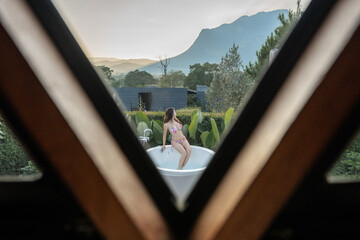 Woman in pink bikini relaxing in the bathtub outdoor.