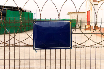 Close-up of blank metal sign on barbed wire fence—captured as editable visual element in secure...
