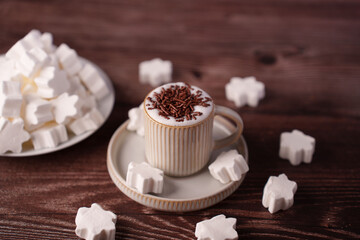 cozy wooden table setting with a ribbed ceramic cup filled with frothy coffee topped with chocolate sprinkles and surrounded by star-shaped marshmallows creating a warm atmosphere, decorative