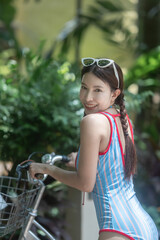 Woman in swimsuit with bicycle, tropical garden background.