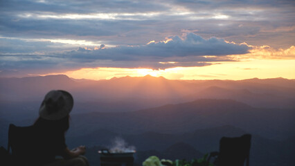 Blurred of a woman cooking and eating Moo Kata, Thai barbecue grill pork with beautiful mountain view before sunset