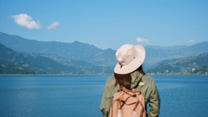 Fototapeta premium Blurred rear view image of a woman looking at a beautiful mountains and the Phewa lake in Pokhara, Nepal