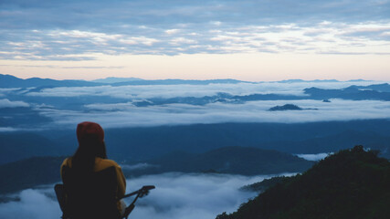 Naklejka premium Blurred rear view of a woman sitting and looking at a beautiful foggy mountain before sunrise