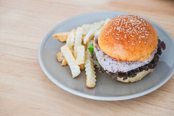 Gourmet burger with a unique purple patty, fresh lettuce, and sesame seed bun served with crispy crinkle cut French fries on a gray plate, Fast Food Meal Concept.
