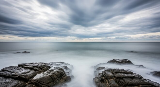 A long exposure of a rocky coastline under a cloudy sky over the ocean - Powered by Adobe