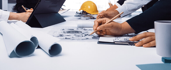 A dynamic design meeting in a modern office where engineers and architects collaborate on blueprints and technical drawings, fostering innovation and teamwork. SACTR