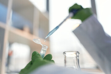Scientist wearing green gloves transferring liquid with pipette into microcentrifuge tube in laboratory setting, conducting scientific experiment