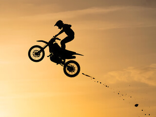 Obraz premium Motocross rider silhouetted against a sunset sky performing a jump motorcycle airborne