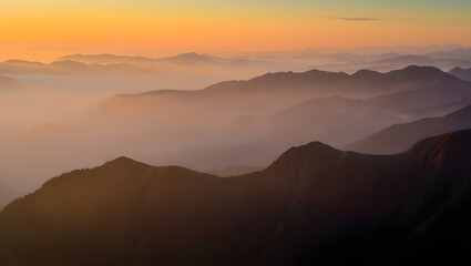 Obraz premium Misty mountain range at sunrise, a breathtaking natural landscape illuminated by golden light