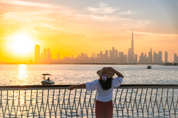 Fototapeta premium young tourist woman watching Dubai skyline at sunset with boats in Dubai creek harbor, solo travel and tourism stock image 