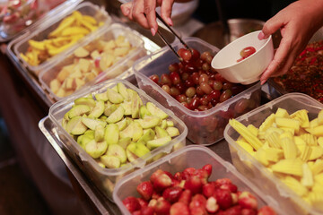 Hand serving fresh tropical fruit from food stall. Delicious asian street food with mango, guava, and plum. An appetizing snack selection at local market
