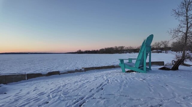 Scenic winter landscape features a vibrant turquoise chair on snow-covered shore, camera pans to reveal tranquil frozen lake and horizon