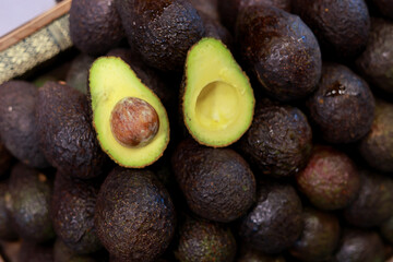 Fresh ripe avocado cut in half, showing its seed and green flesh, sits on large pile of whole...