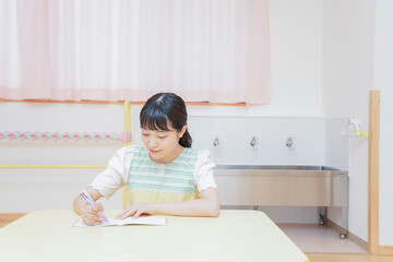 Naklejka premium 事務作業をする若い幼稚園教諭