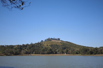 Peaceful landscape with green hill and tranquil lake under clear blue sky. This scenic nature background showcases serene forest by water on bright summer day