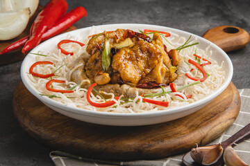 Delicious stir-fried chicken with noodles, garnished with red chilies and green onions, served in a white bowl on a wooden board.