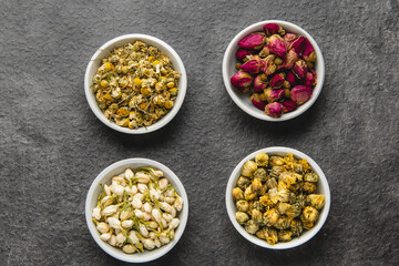 Four bowls of dried chamomile, rose, jasmine, and chrysanthemum flowers for herbal teas or aromatherapy, arranged on a dark background.