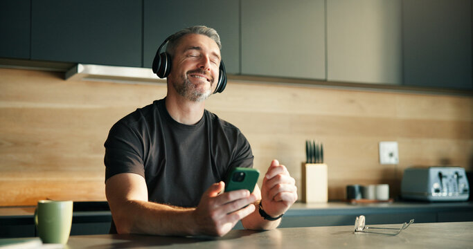 Headphones, streaming or man in home with dance, song connectivity or listening to music playlist. Rhythm, mature or male person in kitchen with tech, feeling beat or radio subscription on audio app. - Powered by Adobe