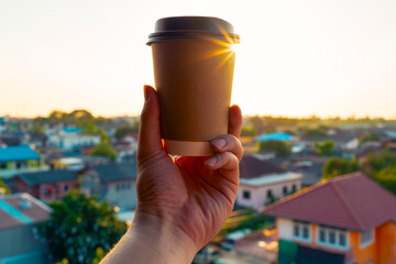 A hand holding a takeaway coffee cup against a warm sunrise over a suburban neighborhood, expressing morning energy, lifestyle routines, relaxation, and the uplifting mood of a new day.