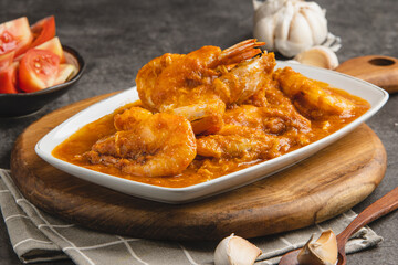 Delicious prawns cooked in a rich, savory orange sauce, served on a white plate with fresh tomatoes and garlic in a culinary setting.