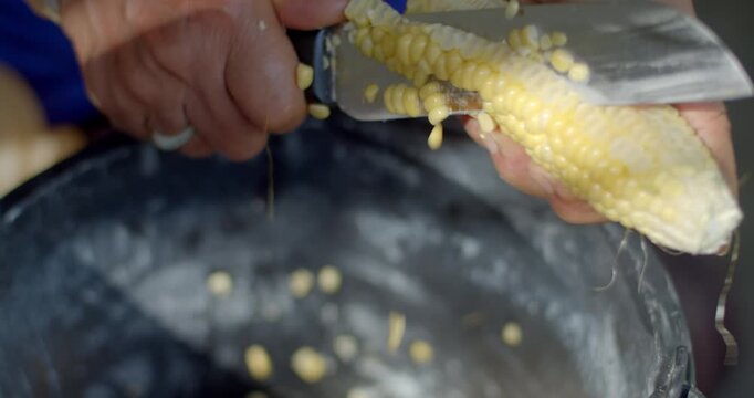 Corn kernels are sliced from fresh corn cobs and collected into a container for use as animal feed, showing a simple agricultural food preparation process.