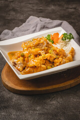 Delicious Asian-style fried chicken or fish coated in a creamy orange sauce with green peas, served in a white bowl on a wooden board.