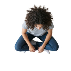 Young person sitting on floor with legs crossed looking down in casual clothes in a bright space