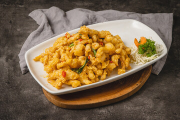 Close-up of a delicious plate of crispy fried chicken or seafood coated in a rich, creamy sauce, garnished with fresh herbs and served on a white rectangular dish.