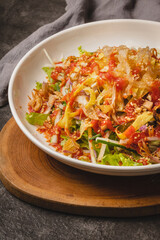 A vibrant salad with fresh greens, shredded egg, and a spicy red dressing, served in a white bowl on a wooden board.