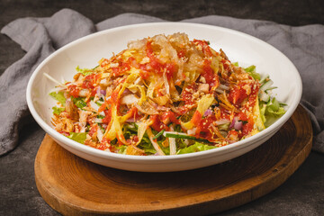 A vibrant and fresh Asian-style salad featuring shredded vegetables, greens, and a spicy dressing, served in a white bowl on a wooden board.