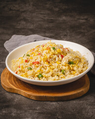 A delicious bowl of homemade fried rice with corn and red bell peppers, served on a rustic wooden board against a dark background.