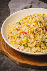 A close-up shot of delicious homemade fried rice with scrambled eggs, red bell peppers, and green onions served in a white bowl on a wooden board.