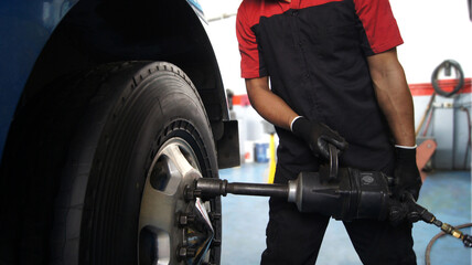 Mechanic changing tires on a truck using a pneumatic impact wrench in an auto repair shop. Close-up...