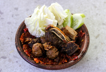 A spicy and savory serving of Iga Bakso Penyet (Smashed Ribs and Meatballs), featuring tender short ribs and bakso pieces smothered in a vibrant red sambal or chili.