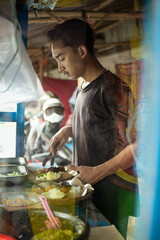 Portrait of young Asian man at work, cooking street food outside. The young man is street food seller of grilled chicken working with his father. Proud of small business owner doing his job.