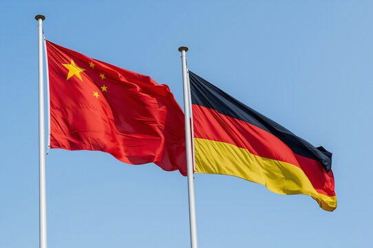 Flags of the people's republic of china and germany waving together against a bright clear blue sky, symbolizing international trade, cooperation, and diplomatic relations.
