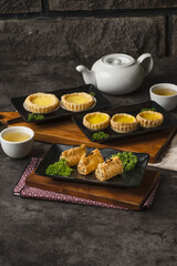 A delightful spread of traditional Chinese dim sum, featuring golden egg tarts and savory fried rolls, served with hot tea on a rustic table.