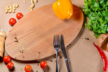 Empty wooden cutting board with knife and fork and vegetables next to it on the table