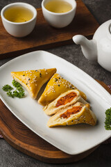 Golden triangular pastries with savory filling served on a white plate with tea.