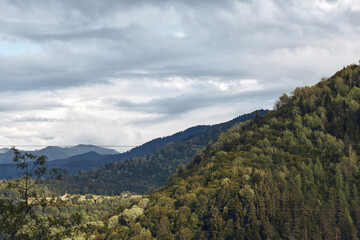 Landscape of rolling hills and dense forest under a cloudy sky conveying calm and natural beauty across the valley and distant mountains inviting exploration and peaceful reflection