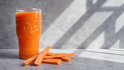 Fresh Carrot Juice in Glass with Sticks on Table with Shadows