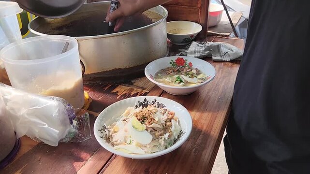 Soto Vendor Pouring Hot Broth into Freshly Prepared Soto Soup. Pouring Hot Soto Soup Broth into Delicious Street Food Bowl. Authentic Soto Soup: Vendor Pours Hot Broth into a Fresh Bowl