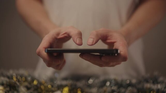Close-up hands of person alpha generation typing fast on smartphone touchscreen, sending messages, connecting with friends and family, celebrating holidays, communicating during festive season.
