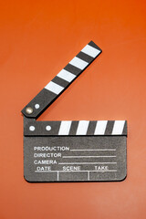 A film clapperboard on an orange background, used in the movie industry. The slate is opened to indicate the start of a film.