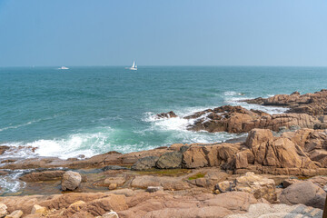 Waves crashing on the shore, Sailing small boats and rocky shores of the Yellow sea in Qingdao, China