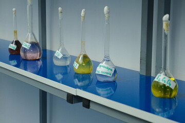 Row of labeled lab flasks with colorful chemical solutions on blue counter, used in scientific experiments.