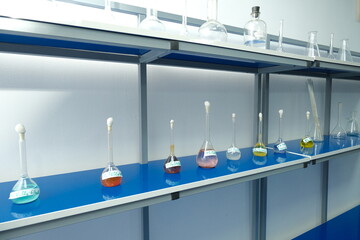 Row of labeled lab flasks with colorful chemical solutions on blue counter, used in scientific experiments.