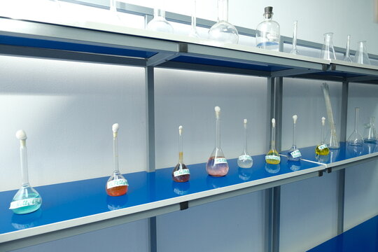Row of labeled lab flasks with colorful chemical solutions on blue counter, used in scientific experiments.