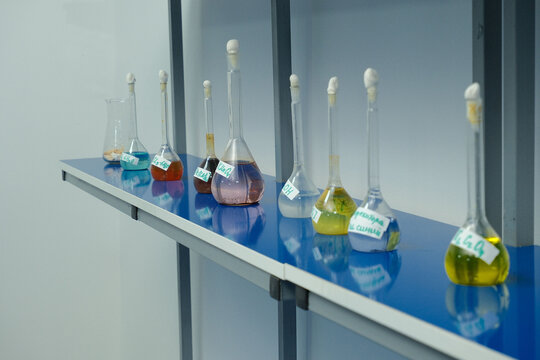 Row of labeled lab flasks with colorful chemical solutions on blue counter, used in scientific experiments.